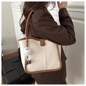 Detalle de bolso tote beige con asas marrones y colgante peludo llevado por una modelo