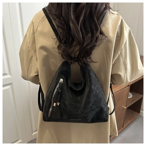 Close-up of black matte bucket bag worn as a backpack with zipper and tassel detail
