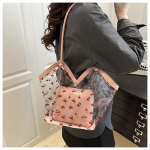 Detail of transparent cherry print tote bag with inner pink pouch shown on model shoulder