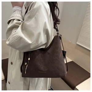 Detail of a dark brown suede tote bag with gold zipper and embossed fashion lettering
