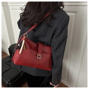 Dettaglio borsa tote bordeaux con pendente in perline di legno e fibbia argentata