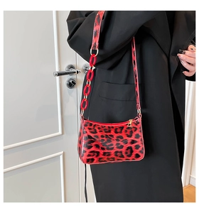 Detail of glossy leopard print shoulder bag with red acrylic chain and gold zipper