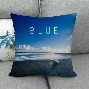 Linen square pillowcase with ocean beach scene and white BLUE text on a grey sofa