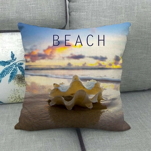 Linen pillowcase with beach sunset print and white seashell on a gray sofa
