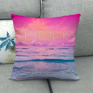 Linen cushion cover with sunset beach scenery and white PINK lettering on a gray sofa