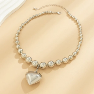 Detailed view of polished silver bead chain with a large 3D heart pendant and lobster clasp