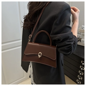 Brown leather crossbody bag with curved base and golden buckle shown on a model