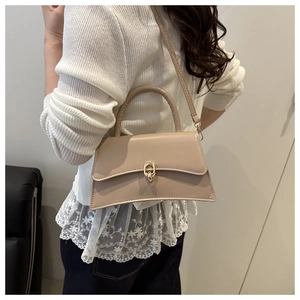 Détail d'un sac bandoulière beige minimaliste avec boucle anneau dorée et base arquée