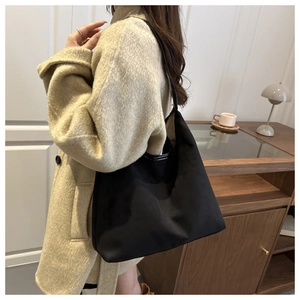 Large black matte tote bag in nylon fabric worn over the shoulder for daily commuting