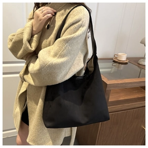 Minimalist black oversized suede tote bag shown on model in a cozy interior setting
