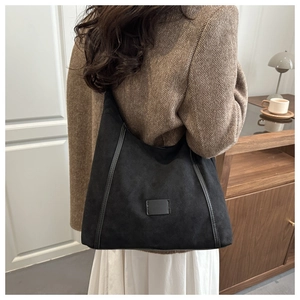 Detail view of large black matte shoulder bag on model with herringbone blazer for workwear