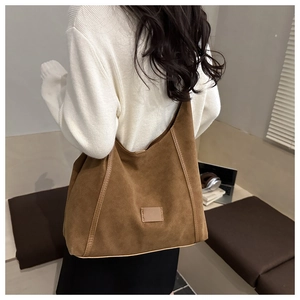 Detailed close-up of brown faux suede tote bag with leather piping and rectangular tag