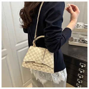 Detailweergave van beige trapeze tas met M-letter prints en gebogen zandloper bodem ontwerp
