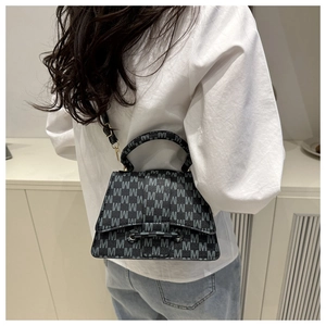 Detail van een trapeziumvormige crossbodytas met M-patroon gedragen door een model