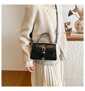 Detail einer schwarzen Steppleder-Handtasche mit goldener Hufeisenschnalle und Flechtmuster