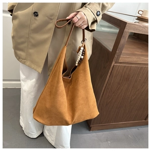Detail of camel suede tote bag featuring dark brown handles and wooden bead pendant