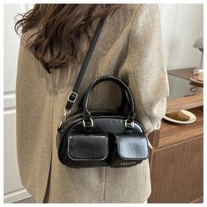 Detail of black leather handbag featuring dual front pockets and gold fashion lettering