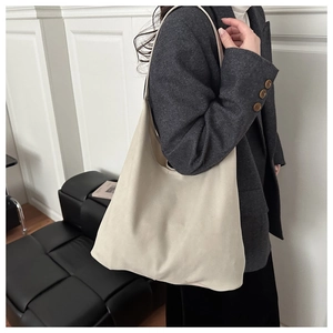 Large beige canvas tote bag with wide shoulder strap shown on a model in a minimalist room