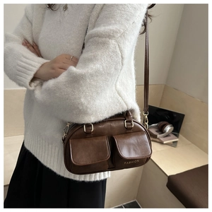 Close-up of brown vintage leather shoulder bag featuring dual front pockets and metal hooks