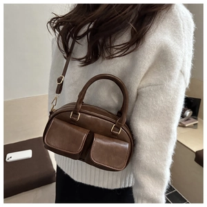 Detail of dark brown vintage cylinder bag showing PU leather texture and dual front pockets