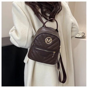 Detail of dark brown mini backpack featuring V-shaped chevron quilting and golden M logo