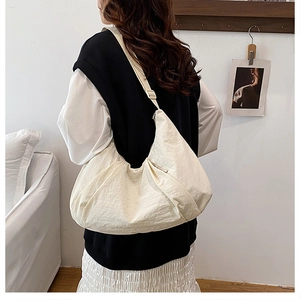 Side view of a large cream nylon crescent bag with adjustable wide shoulder strap on model