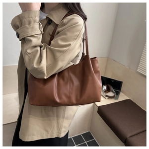 Brown tote bag on model shoulder with professional office background and accessories