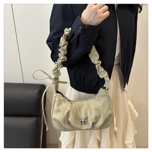 Detail of light green pleated shoulder bag featuring a silver metal butterfly ornament