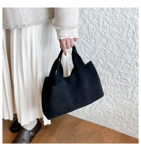 Close-up of minimalist black matte tote bag held by model wearing a chic white outfit