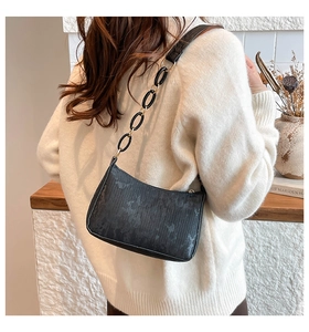 Close-up of black textured leather underarm bag with stylish chain strap on model