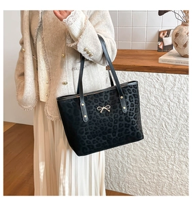 Detail of black leopard print tote bag with gold bow charm and metallic rivets