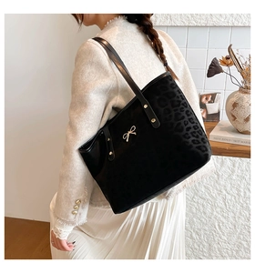Detail of black tote bag with matte finish featuring golden bow and leopard embossed texture