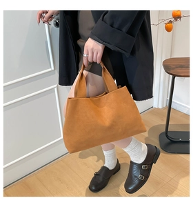 Close-up of a brown suede tote bag with wide straps shown in a warm indoor setting