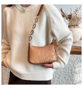 Detail of a brown textured underarm bag with metal chain strap on a model