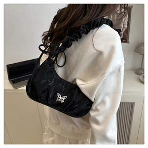 Detail of black pleated shoulder bag with silver butterfly and scrunchie strap on model