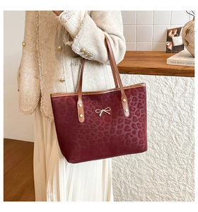 Deep red leopard print tote bag with gold bow pendant on a shoulder strap