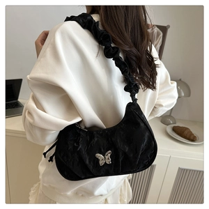 Black ruched shoulder bag with silver butterfly buckle shown in a lifestyle setting