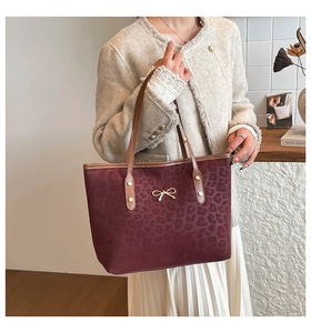 Detail of burgundy leopard print tote bag with gold bow and brown leather handles