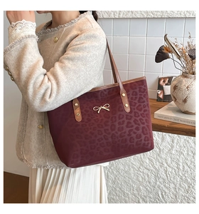 Detail of burgundy leopard print tote bag with golden bow hardware and slim strap