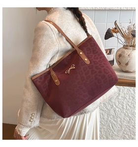 Detail of burgundy leopard print tote bag with golden bow and brown leather strap