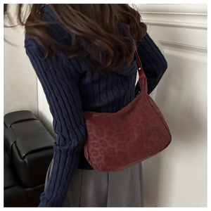 Detail of burgundy leopard print hobo bag with adjustable red shoulder strap worn by model