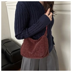 Close-up of burgundy suede shoulder bag with subtle leopard print on a female model
