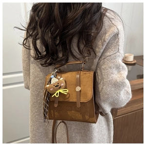 Brown suede mini backpack detail with bear charm and embossed logo on model's back