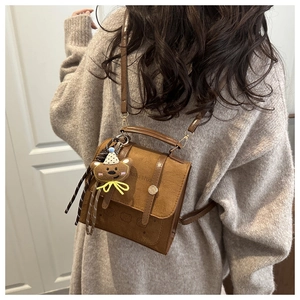 Detail of a brown vintage crossbody bag with bear charm and metallic chain strap