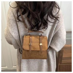 Close-up of brown suede textured backpack with flip-top cover and gold buckle details