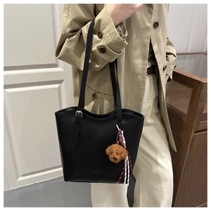 Detail of black leather tote bag featuring a cute brown plush dog charm and shoulder strap