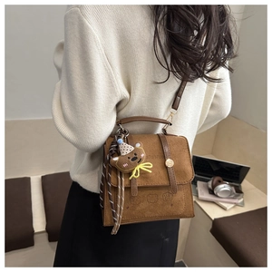 Detail of a brown suede crossbody bag featuring a bear embossment and plush charm
