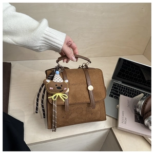 Detailed macro view of brown suede handbag with cute bear charm and logo embossing
