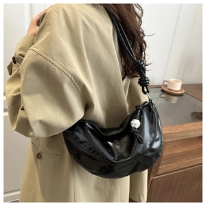 Détail d'un sac demi-lune noir brillant avec bandoulière nouée et pendentif à billes blanches
