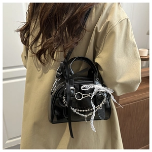 Detail of black glossy handbag with lace bows and silver chains worn by model